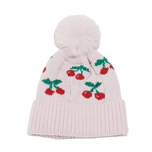 Detail of pink knit beanie featuring red cherry patterns and a large fluffy pom-pom top