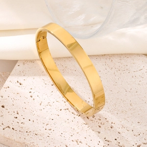 Minimalist gold-plated wide bangle featuring a smooth polished finish on a stone display
