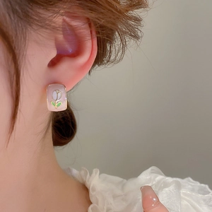 Close-up of a pink enamel square earring with a white tulip pattern and gold plating