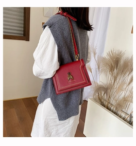 Close-up of red leather crossbody bag with vintage metal bee buckle and rivet details