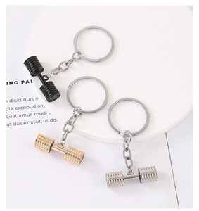 Black, gold and silver dumbbell keychains on a white circular plate for fitness lovers