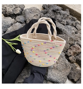 Detail of handmade straw bucket bag with colorful pom-poms and twisted rope handles