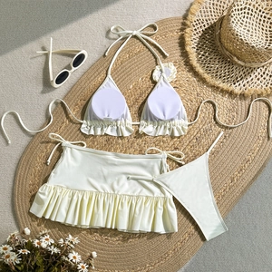 Flat lay of off-white three-piece bikini set with ruffle skirt on a woven beach mat