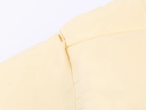 Close-up of pale yellow quilted jacket showing seam stitching and thick padding details