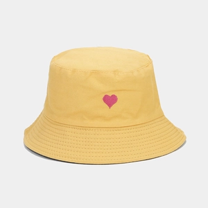 Détail de la broderie cœur rose et des coutures parallèles sur un chapeau bob en coton jaune