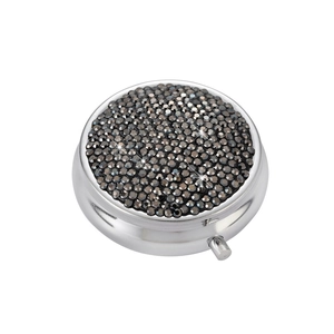Detail of round silver pill box with shimmering black rhinestones and side push-button latch