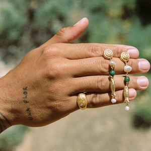 Close-up of bohemian gold fish earrings with pearls and a textured gold ring on hand