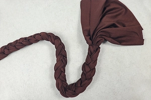 Detailed view of dark brown knitted headband with woven strap on textured surface