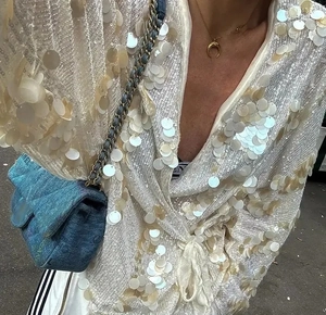 Detail of long sleeve top with beige sequins paired with blue denim chain bag