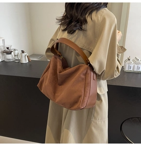 Deep brown suede baguette bag shown on shoulder over a trench coat in a cafe