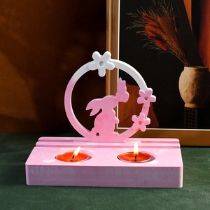 Macro detail of a rabbit-shaped tea light candle holder with lit candles on a green desk