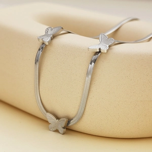 Detailed macro view of silver snake chain with delicate butterfly charms on a stand