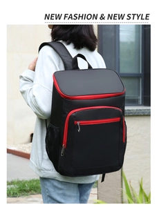 Detail of a black insulated picnic backpack with red zipper accents worn by a model outdoors