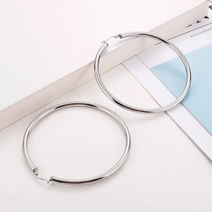 Close-up of polished silver titanium steel hoop earrings on a minimalist white surface