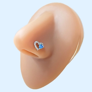 Macro shot of a heart-shaped nose stud with blue opal and white zircon on a model nose