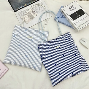 Detail of checkered canvas tote bag featuring delicate blue bow embroidery and brand tag