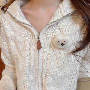 Detail of cable knit white cardigan with soft plush monster patch and silver zipper