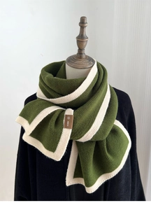 Detail shot of green knit scarf with white stripes and a leather brand label