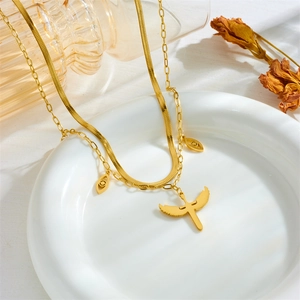 Detail of gold layered necklace with snake chain and winged cross pendant in a ceramic bowl