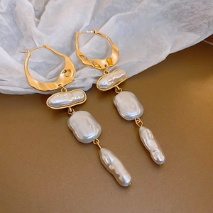 Detail of baroque pearl tassel earrings with gold irregular rings on elegant background