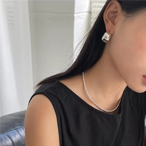 Close-up of a model wearing minimalist silver square stud earrings and a thin bead necklace