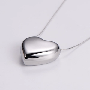 Close-up of polished silver heart pendant with minimalist snake bone chain necklace
