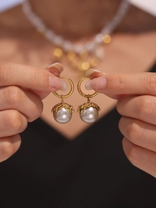 Detail of elegant gold-plated flower hoop earrings featuring large grey shell pearls