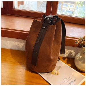 Detail of caramel suede bucket bag with leather strap on a textured wooden surface