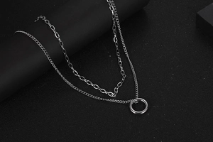 Detail of layered silver chain necklace with a ring pendant on a black textured background