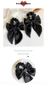 Detail of elegant black satin bow hair scrunchie with handmade tag and long ribbons
