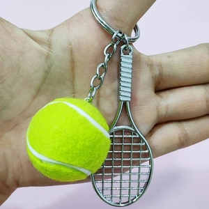 Close-up of yellow tennis ball and silver metal racket keychain held against pink background