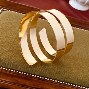 Detailed close-up of a wide multi-layered gold spiral cuff bracelet on a green velvet stand