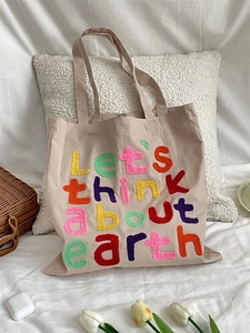 Beige canvas tote bag with rainbow chenille embroidery lettering on a white pillow