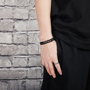 Close-up of black Cuban link chain bracelet worn on wrist against a gray wall