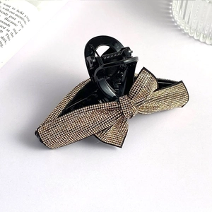 Detail of black bow hair claw clip with golden rhinestones on an elegant background