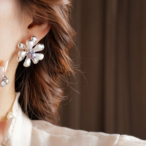 Close-up of 18k gold plated flower stud earring with silver needle and purple bead center