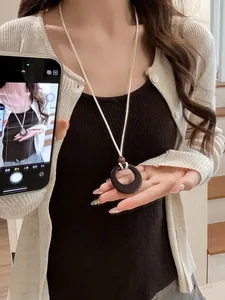 Detail of a minimalist black resin ring pendant on a cream-colored cord worn by a model