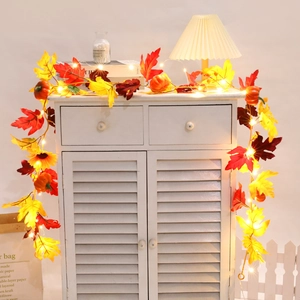 Detail of autumn maple leaf garland with mini pumpkins and warm LED lights on a white cabinet