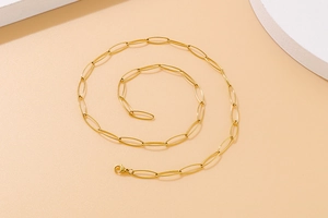 Macro shot of gold-plated paperclip chain necklace with lobster clasp on beige background