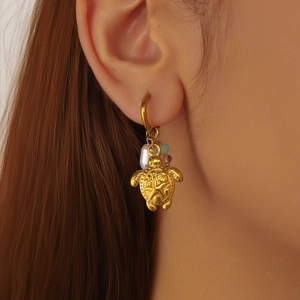Golden turtle drop earrings with pearls and starfish detail worn by a female model