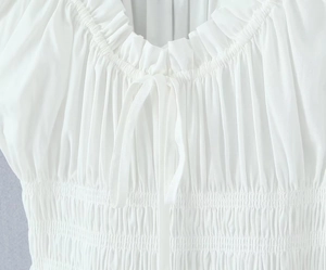 Détail de l'encolure blanche à volants avec smocks élastiques et nœud délicat à cordon