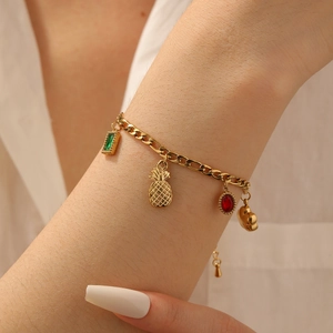 Close-up of gold-plated bracelet featuring cherry, pineapple and gemstone pendants