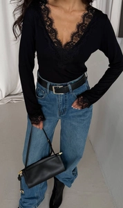 Detailed view of women's black V-neck lace patchwork top paired with casual blue jeans