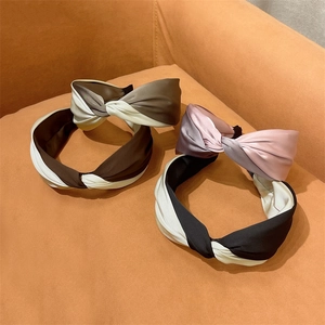 Elegant twist knot headband in two-tone silk satin texture displayed on a fabric surface