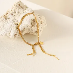 Macro view of gold triple-layer chain bracelet with tassel detail on white stone stand