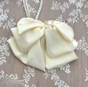 Detail of cream white satin bow hair claw clip with elegant pearl chain on lace background
