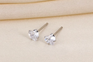Macro shot of heart-shaped zircon stud earrings with classic claw setting on yellow silk