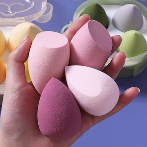 Hand holding four soft pink and purple makeup sponges in teardrop and slanted shapes