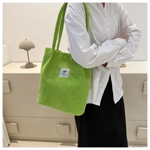Detail of green corduroy bucket bag with white slogan label worn by a model