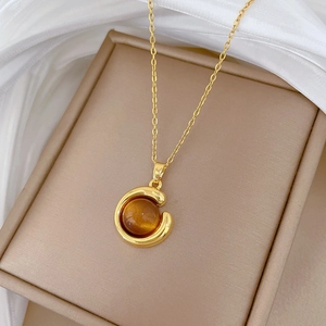 Detail of gold geometric necklace featuring a round amber gemstone in a C-shaped frame